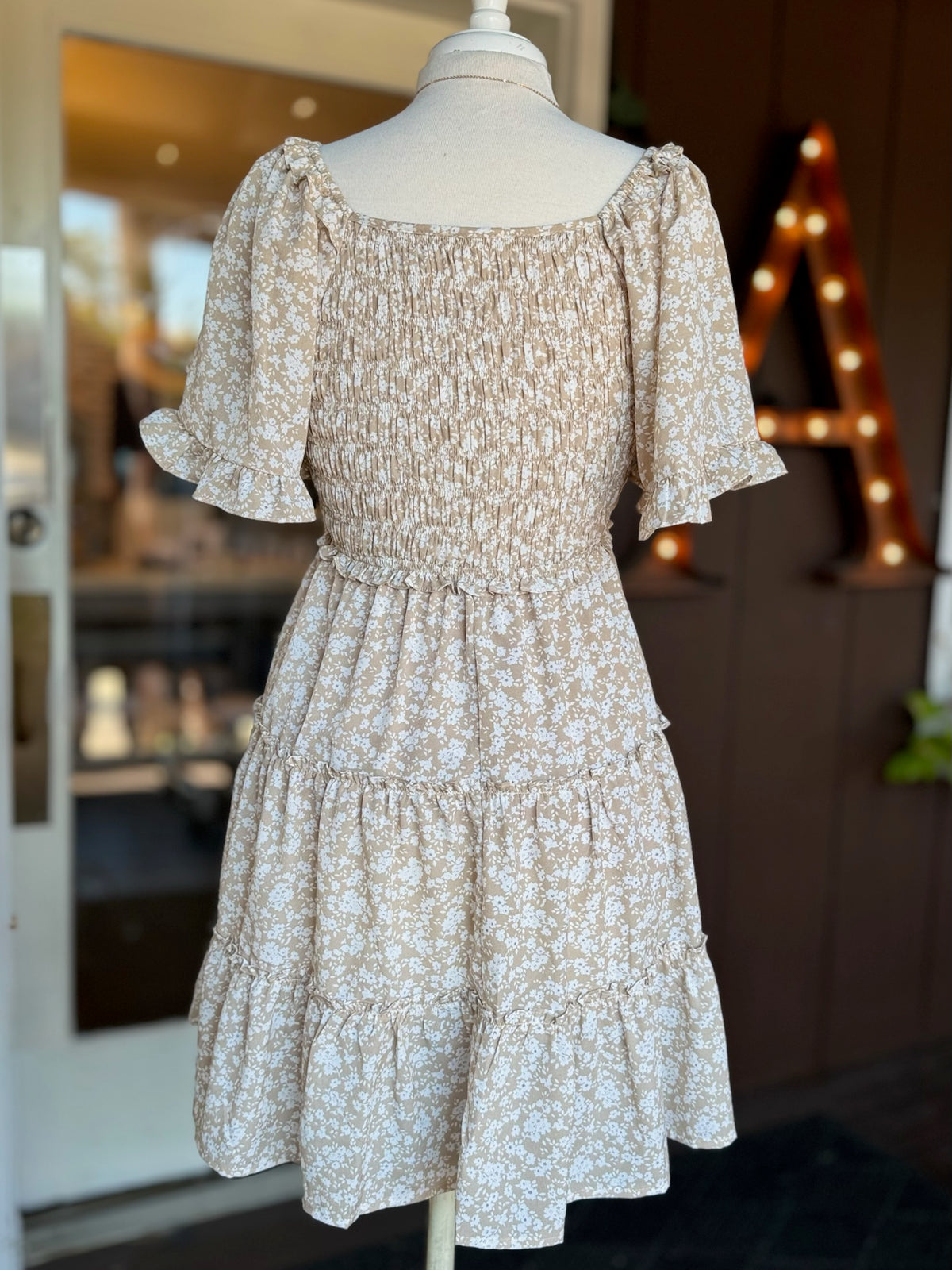 Back view of beige and white floral dress showing the smocked bodice, short flutter sleeves and tiered skirt at Ardor Boutique.
