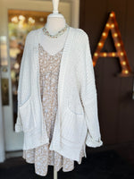 Beige and white floral dress layered with a white open-front knit cardigan for a cozy transitional look at Ardor Boutique.