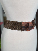 Close-up of brown and bronze beaded stretch belt with oversized wood-look buckle and stud details at Ardor Boutique.