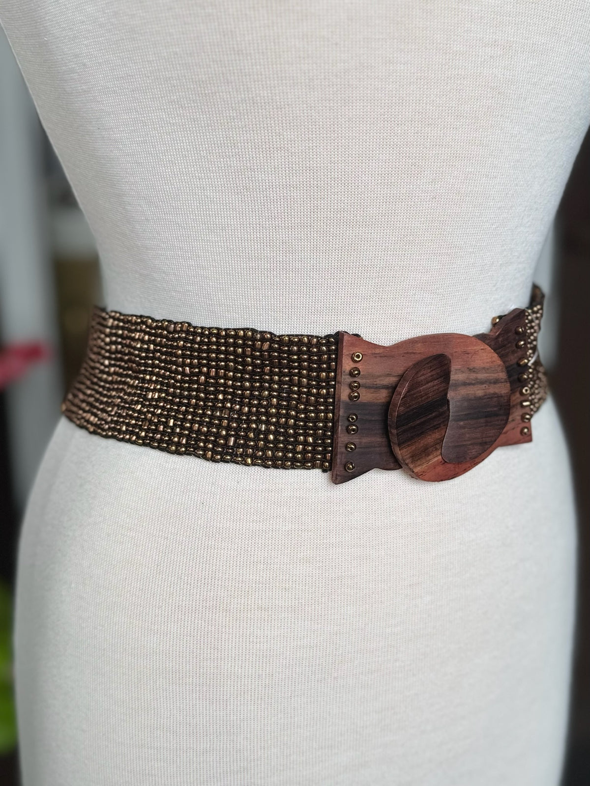 Close-up of brown and bronze beaded stretch belt with oversized wood-look buckle and stud details at Ardor Boutique.
