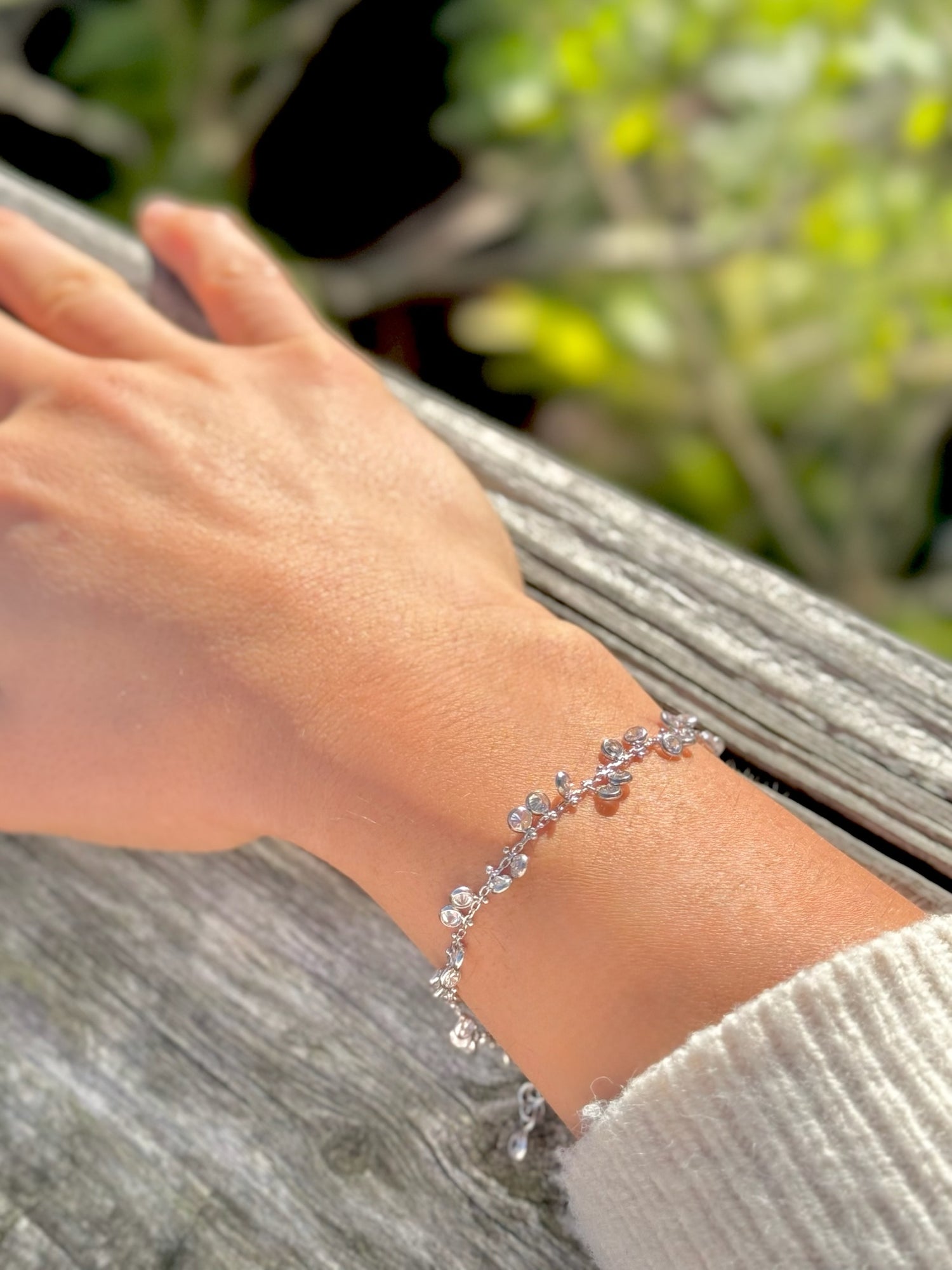Hand wearing a silver bracelet with a blurred natural background