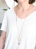 Model wearing gold and labradorite necklace with oval rings and purple amethyst pendant, styled with a white top for a minimalist look.