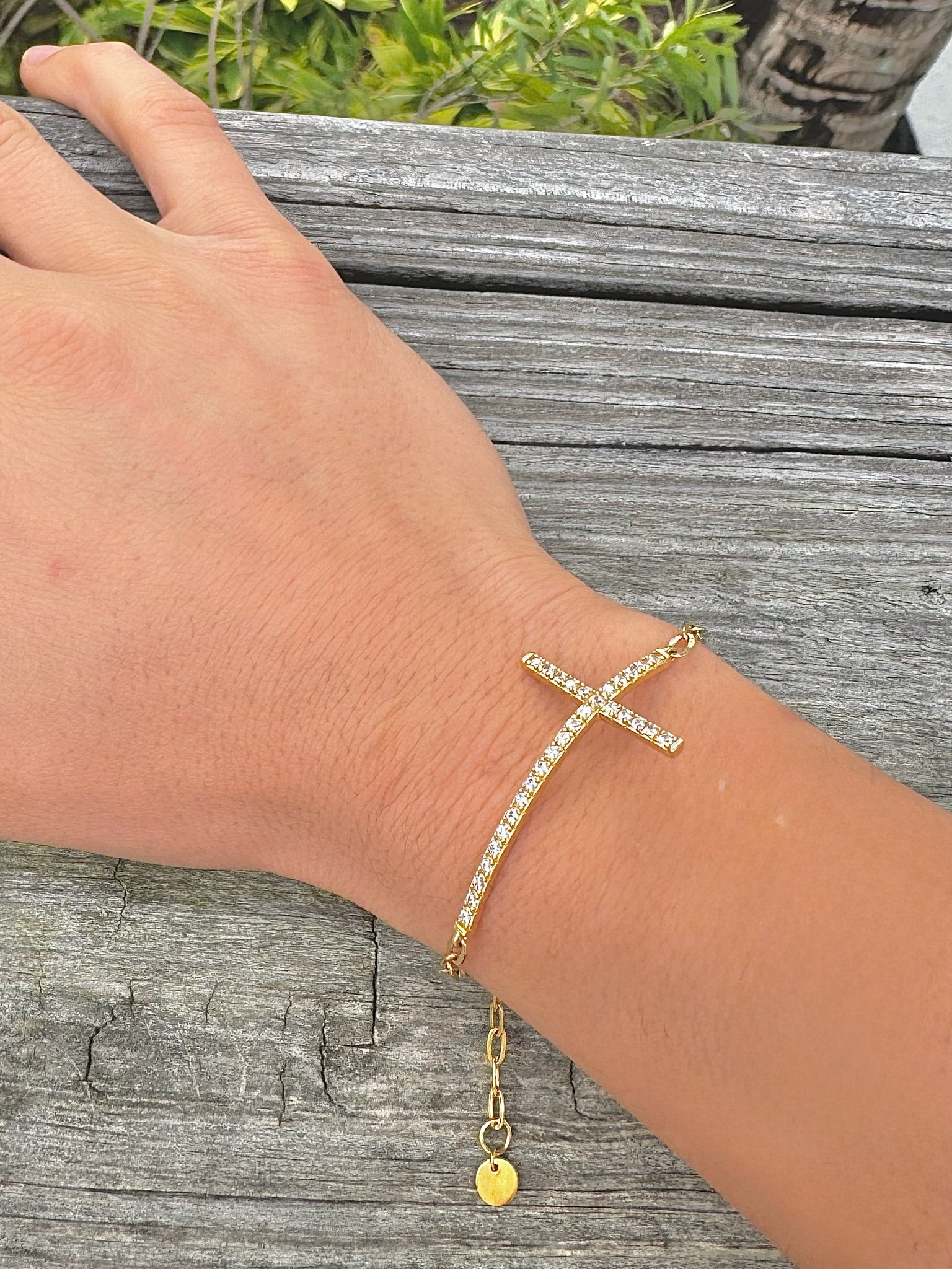 Gold bracelet with a cross design on a wrist against a wooden background