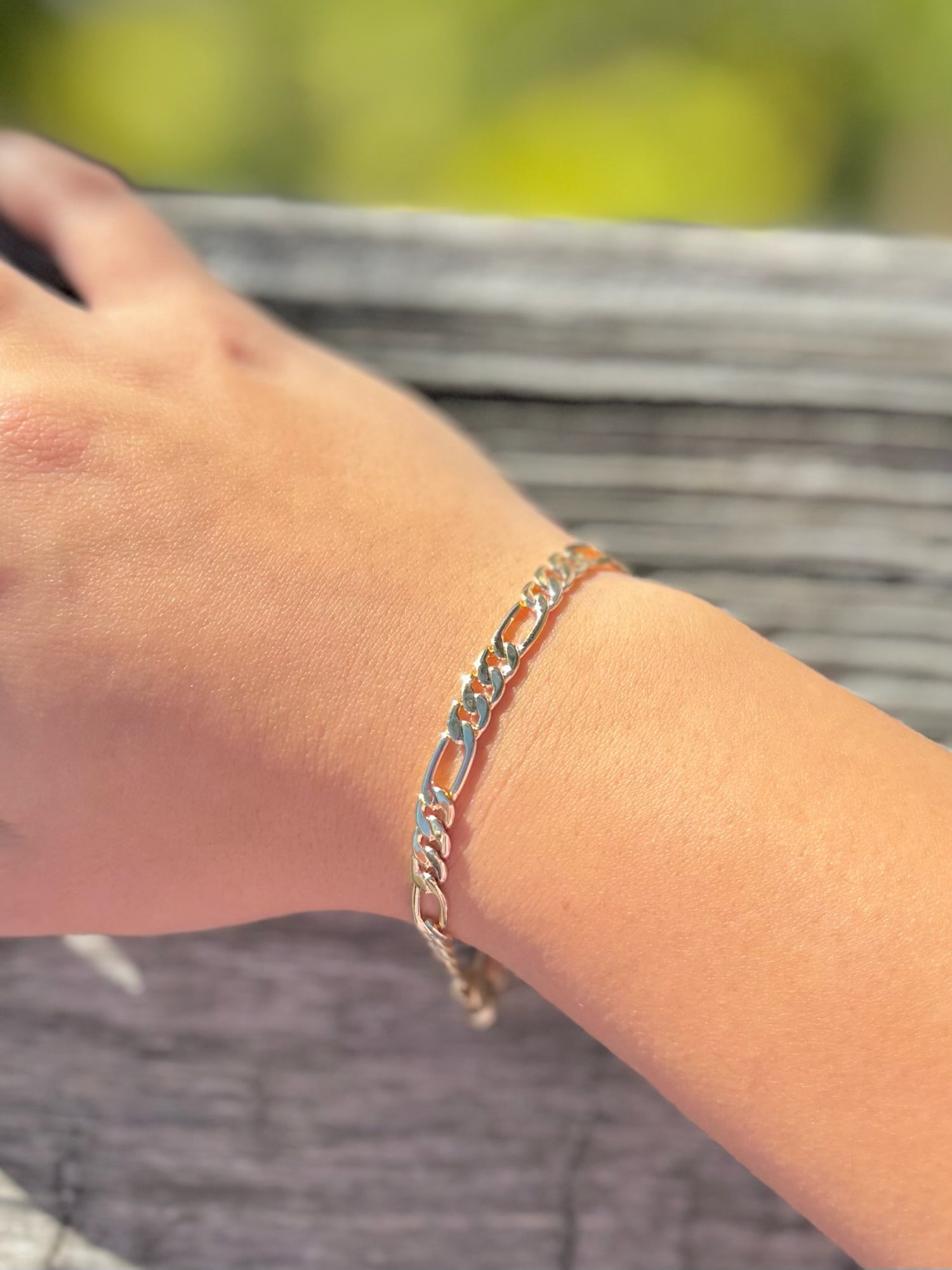 Gold bracelet on a wrist with a blurred natural background