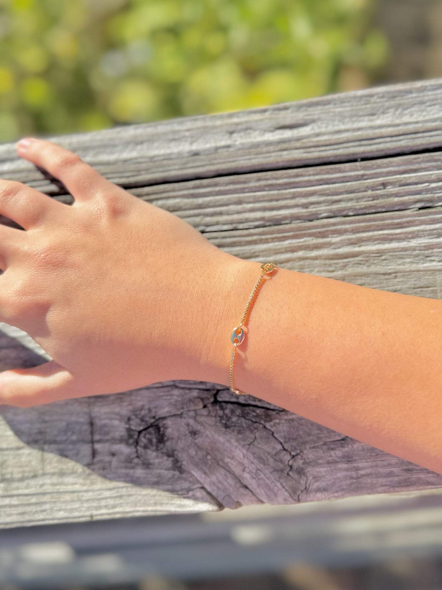 Hand wearing a bracelet on a wooden surface with a blurred natural background