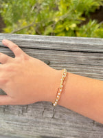 Gold bracelet on a wrist with a blurred natural background