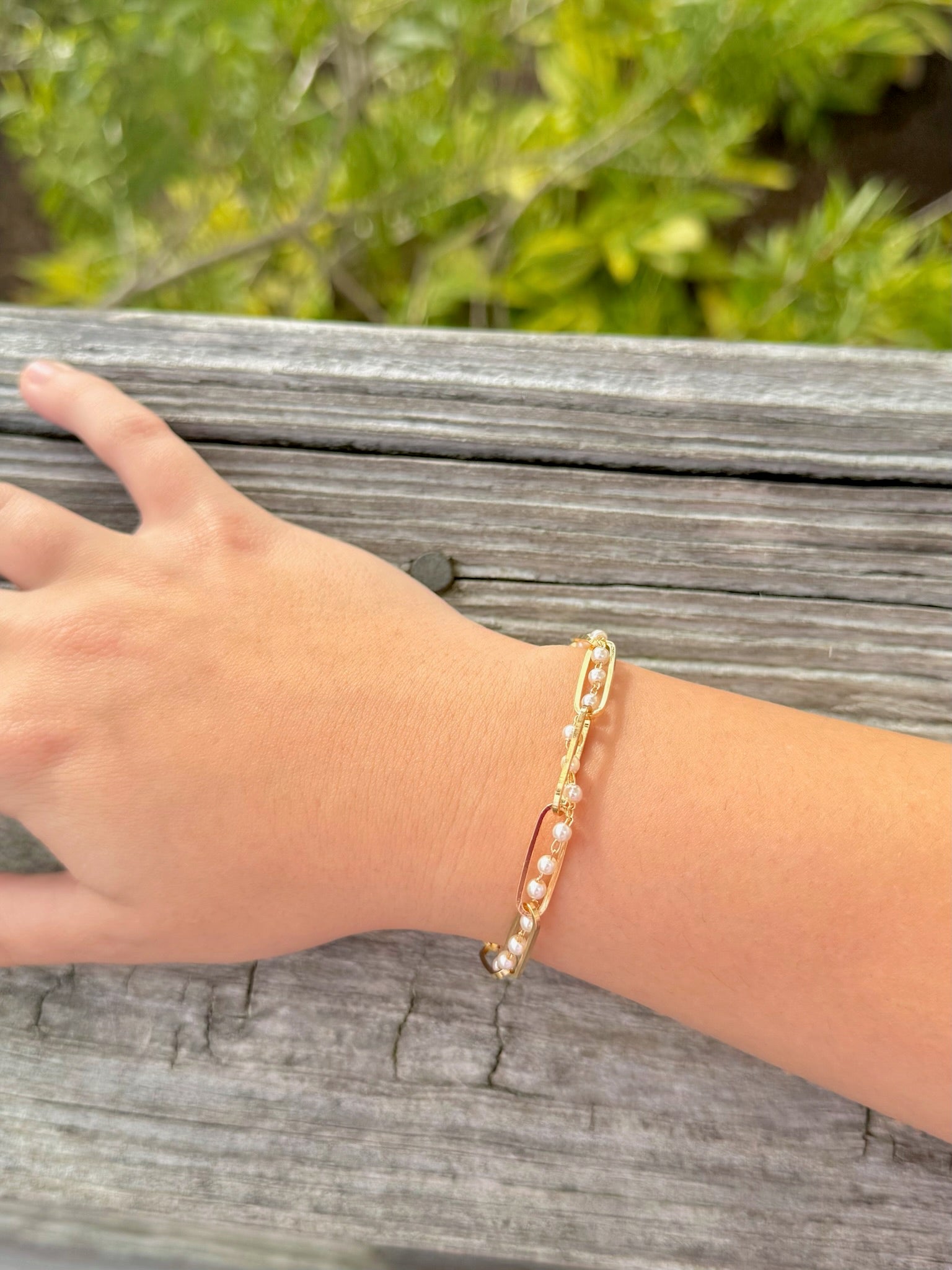 Gold bracelet on a wrist with a blurred natural background