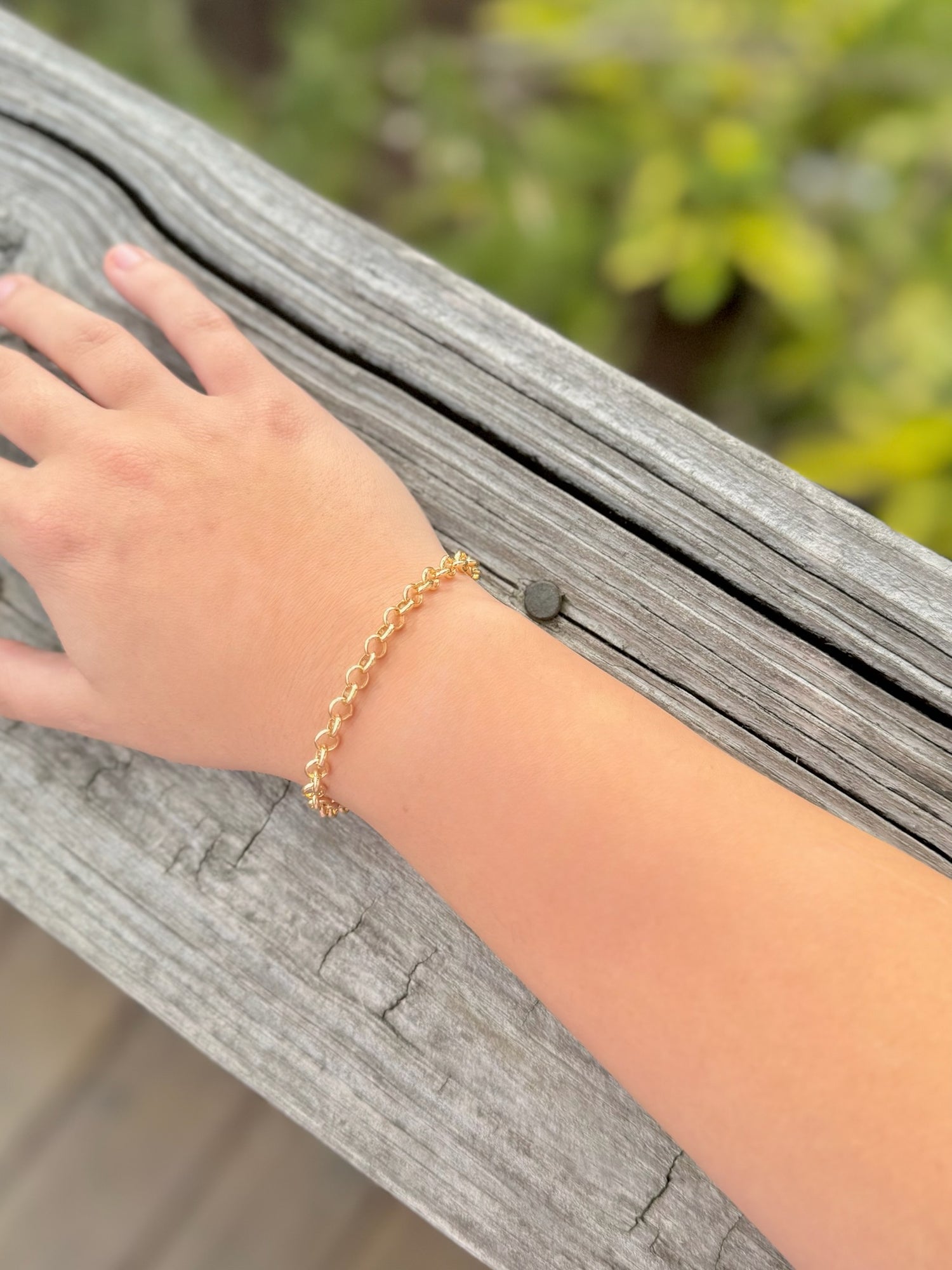 Gold bracelet on a wrist with a blurred natural background
