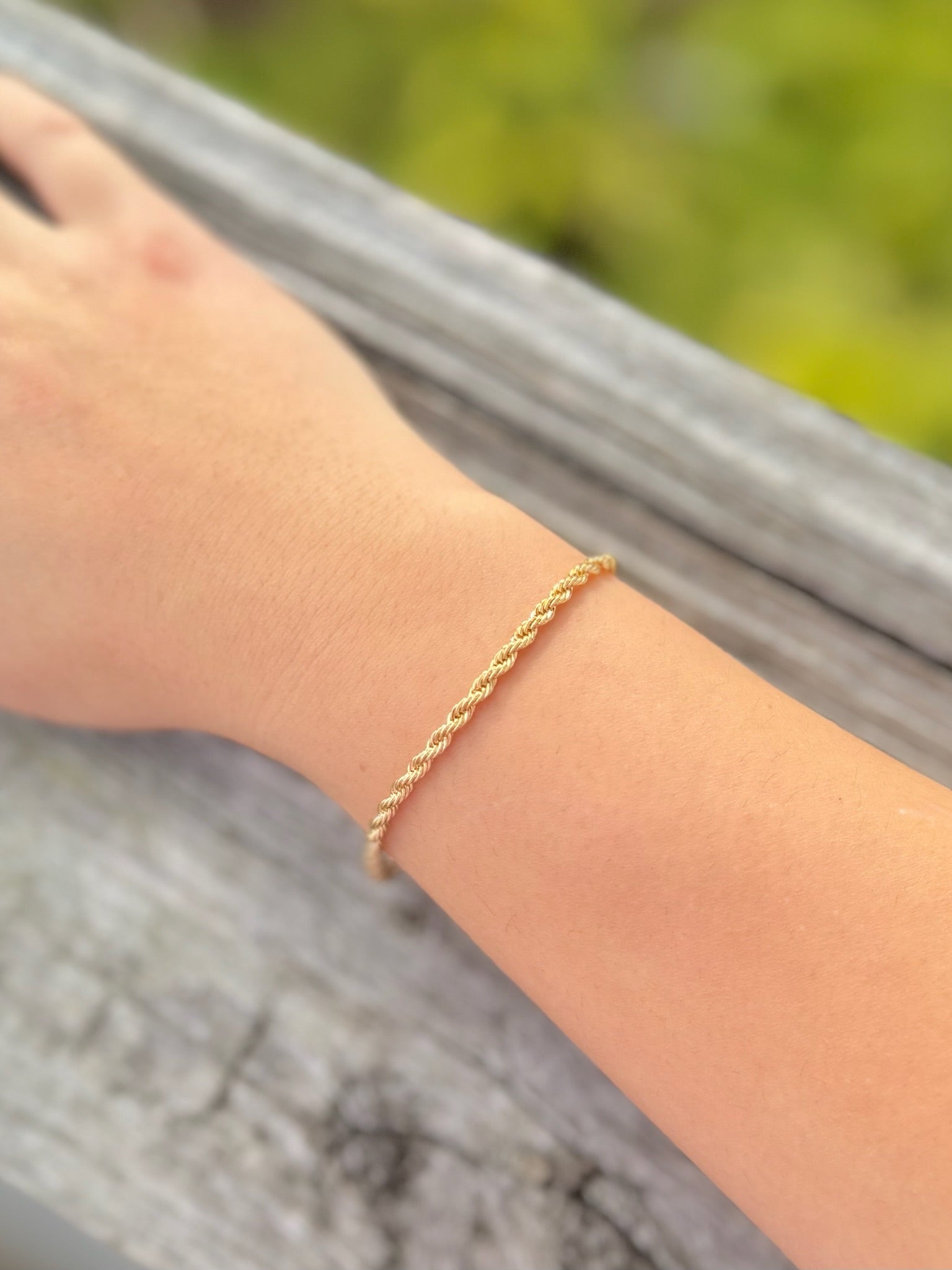 Gold bracelet on a wrist with a blurred natural background