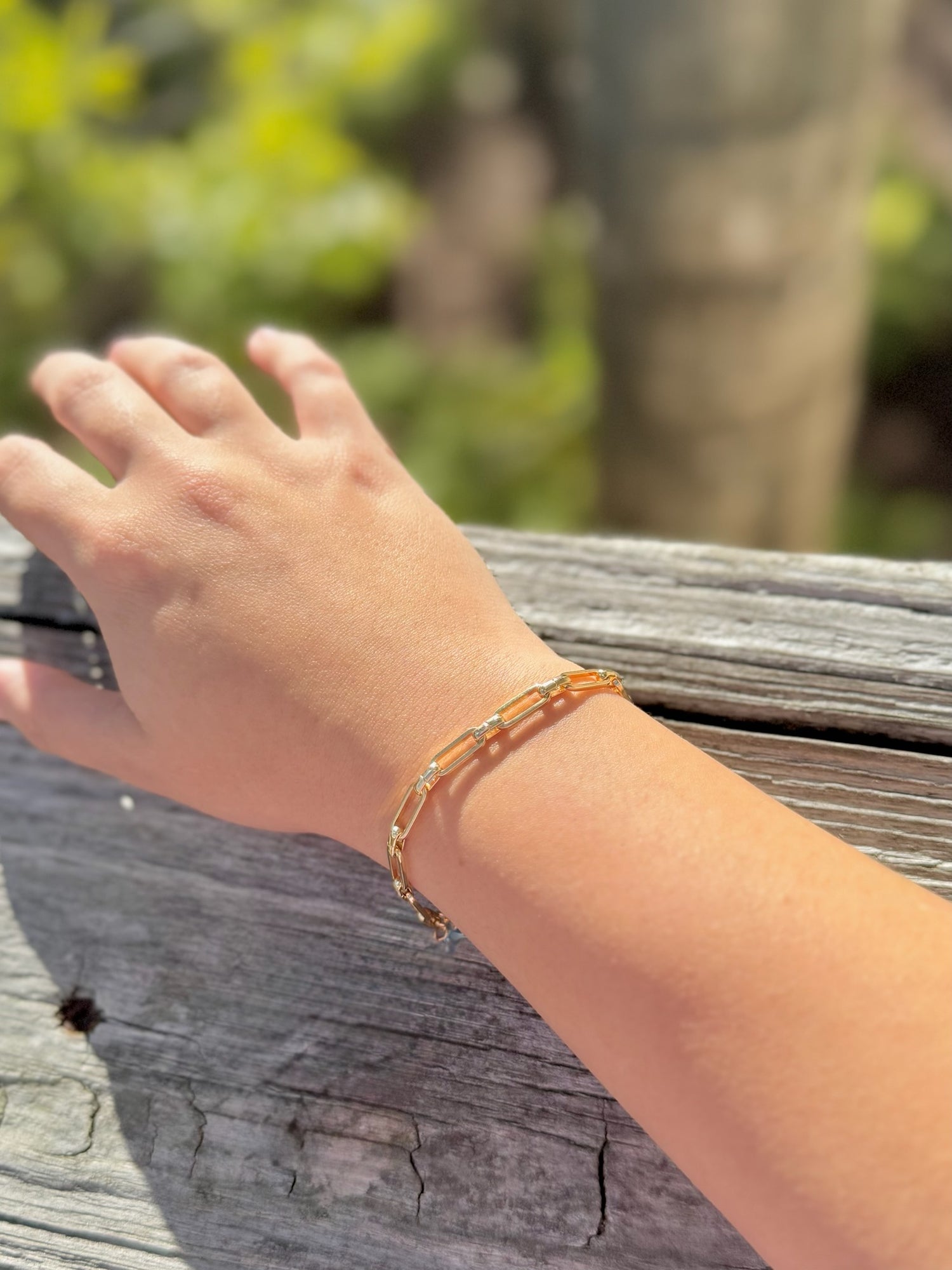 Hand wearing a bracelet on a wooden surface with a blurred natural background