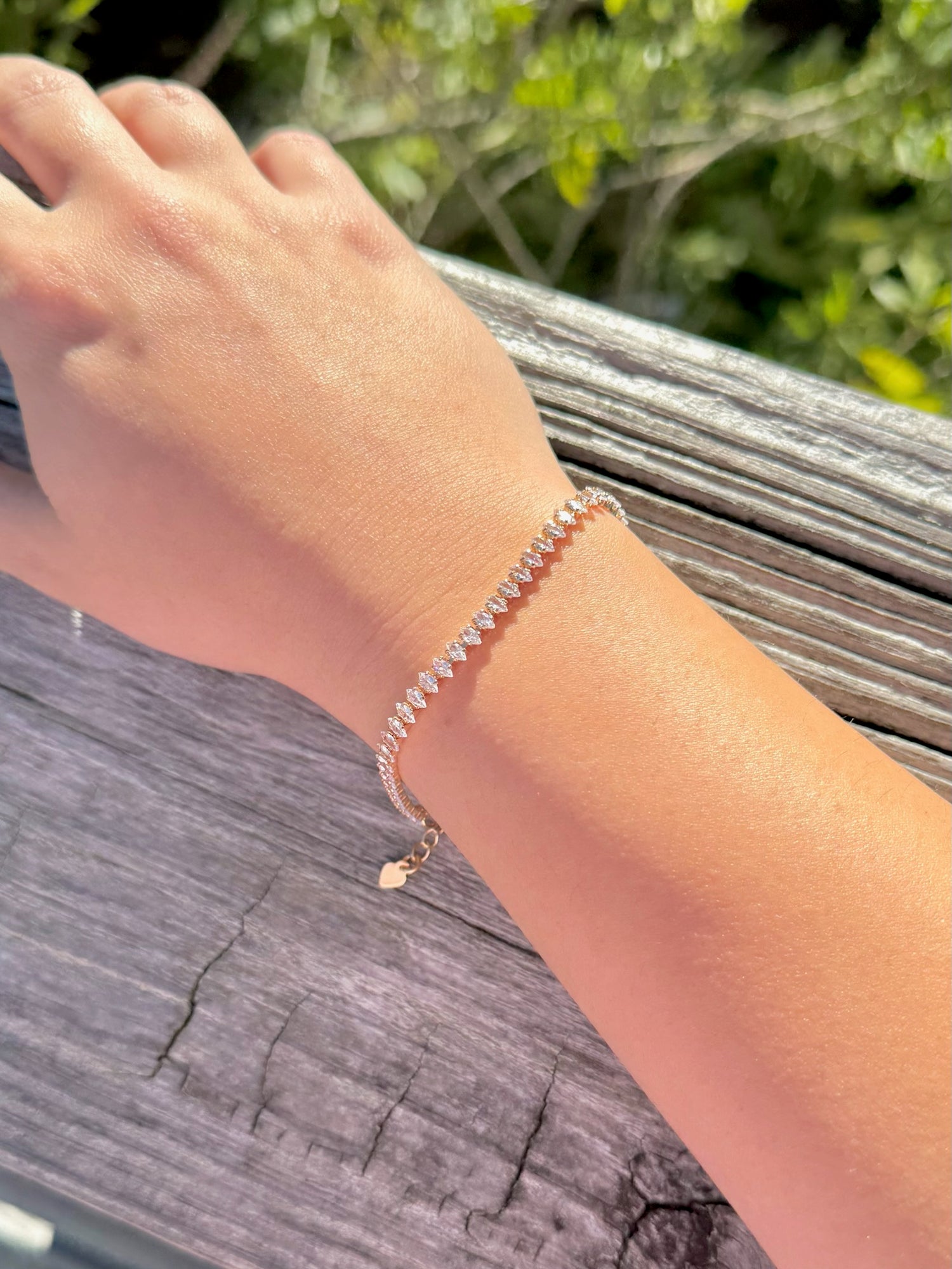 Hand wearing a sparkly bracelet on a wooden surface with greenery in the background
