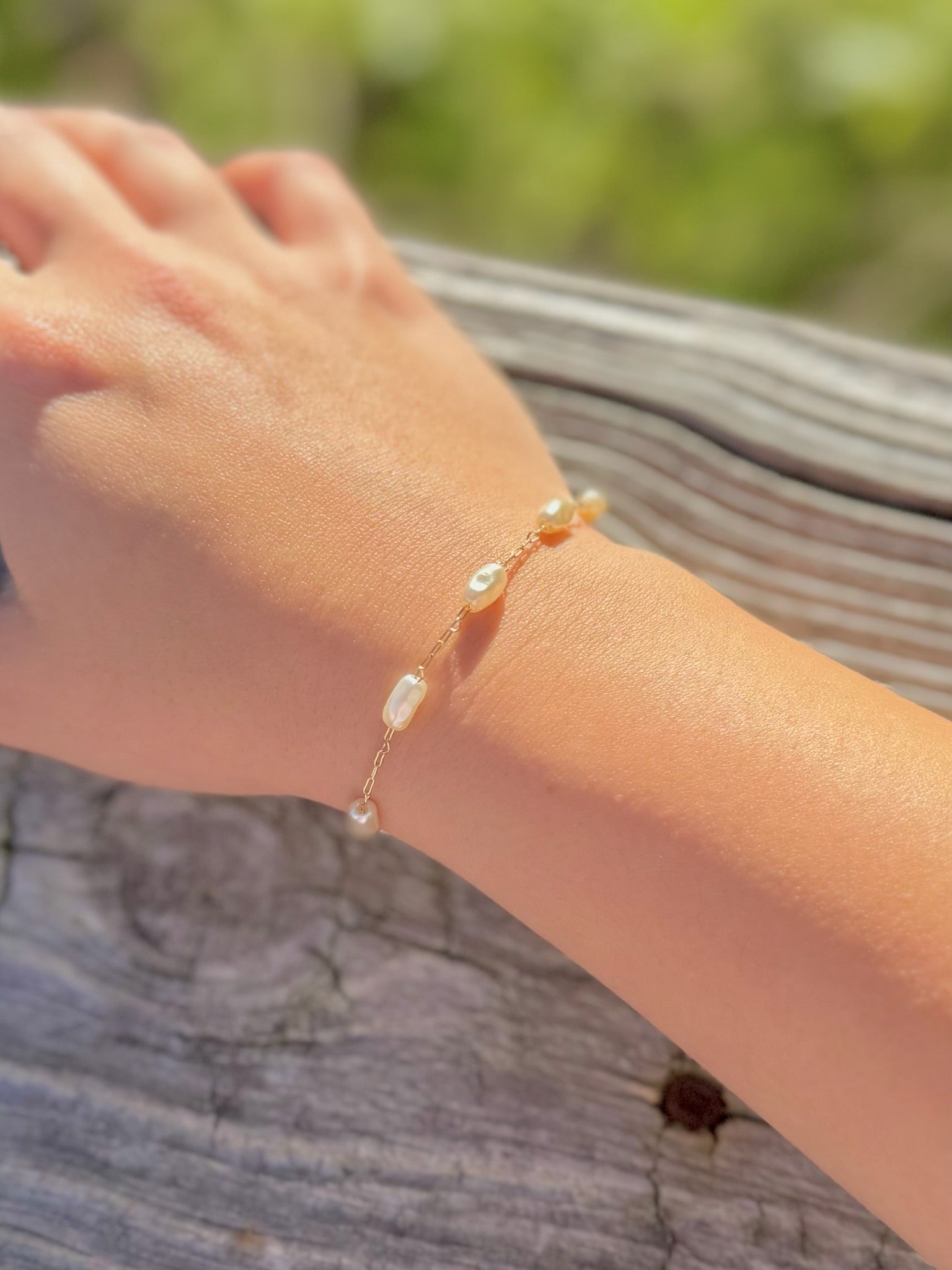 Hand wearing a pearl bracelet with a blurred natural background