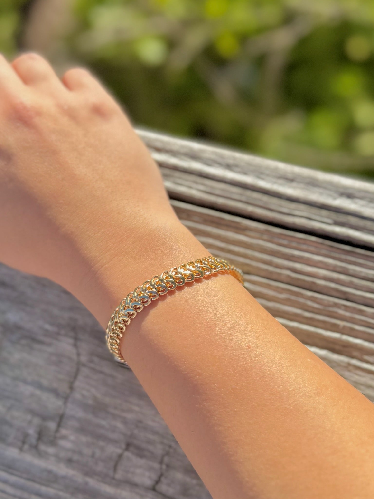 Gold bracelet on a wrist with a blurred natural background