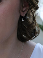 Close-up of a person wearing a delicate silver earring and necklace.