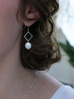 Close-up of a person wearing a silver earring with a pearl pendant.