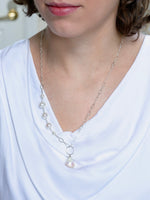 Close-up of a necklace with a pearl pendant worn by a person in a white top.