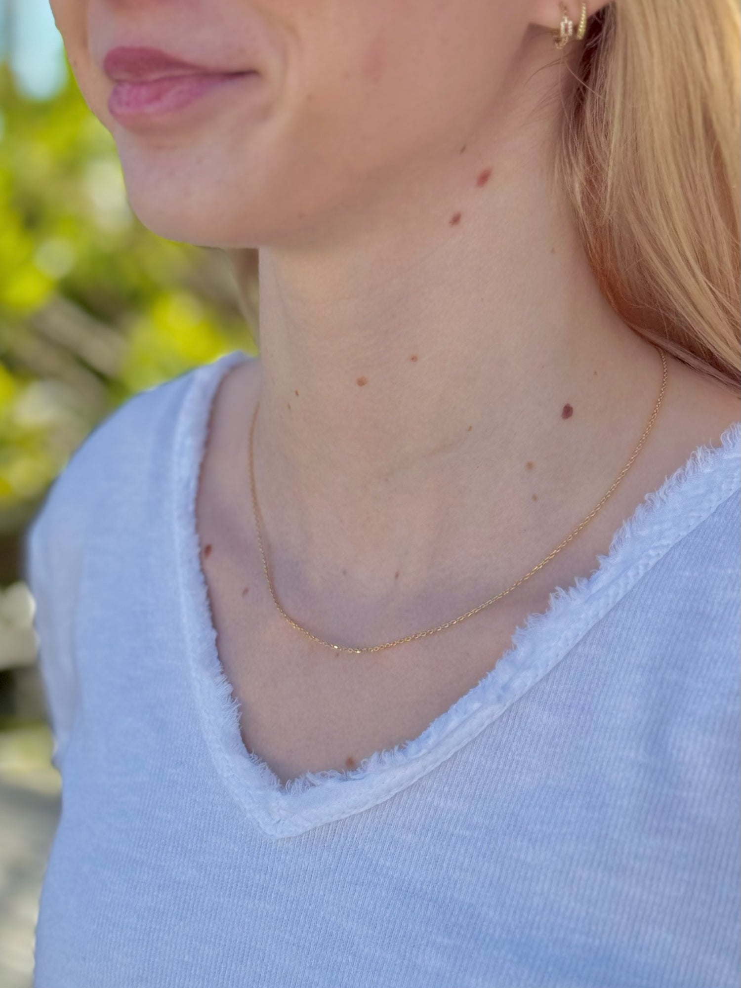 Close-up of a person wearing a delicate gold necklace with a blurred natural background