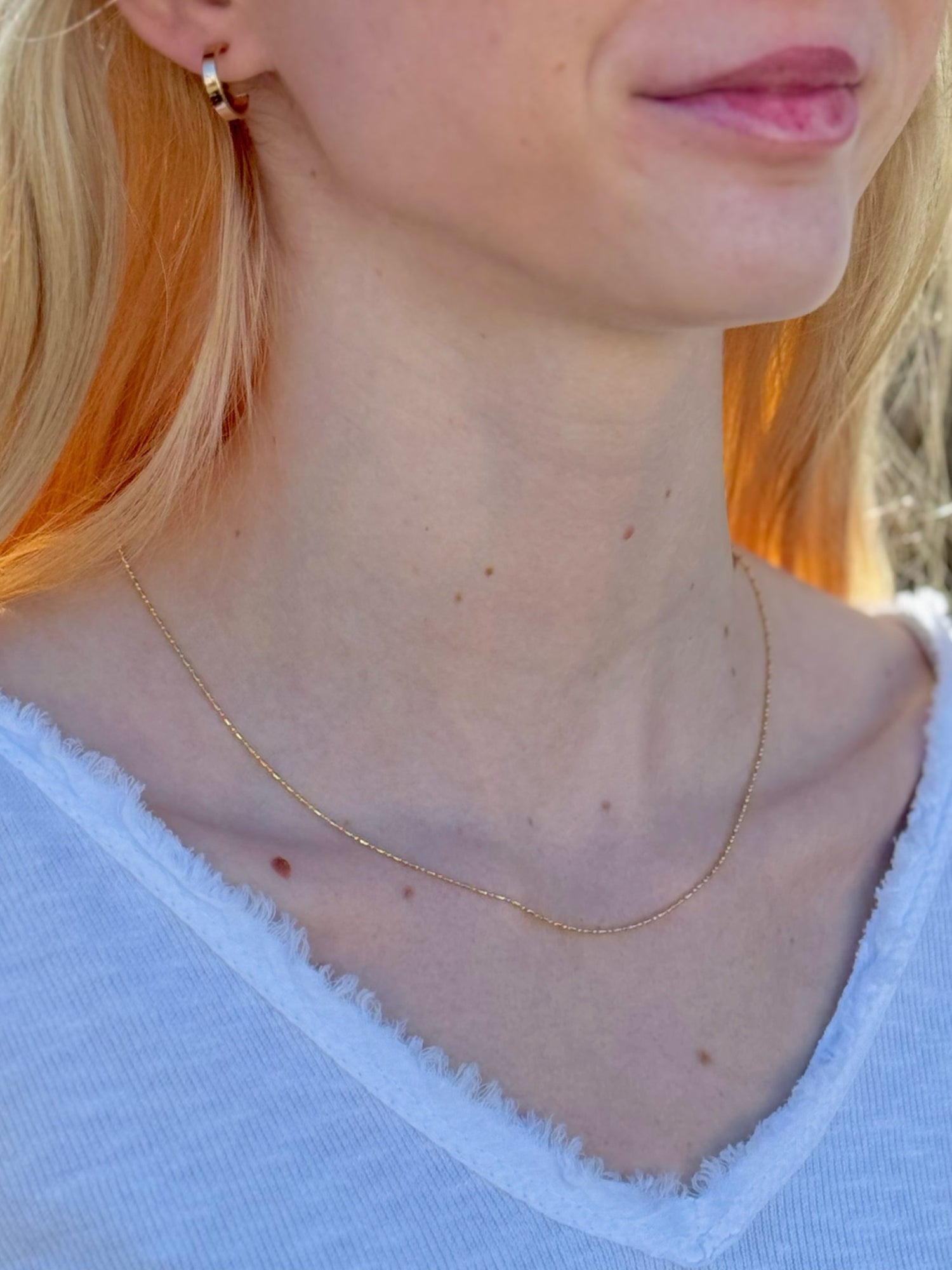 Close-up of a person wearing a gold necklace with a blurred background