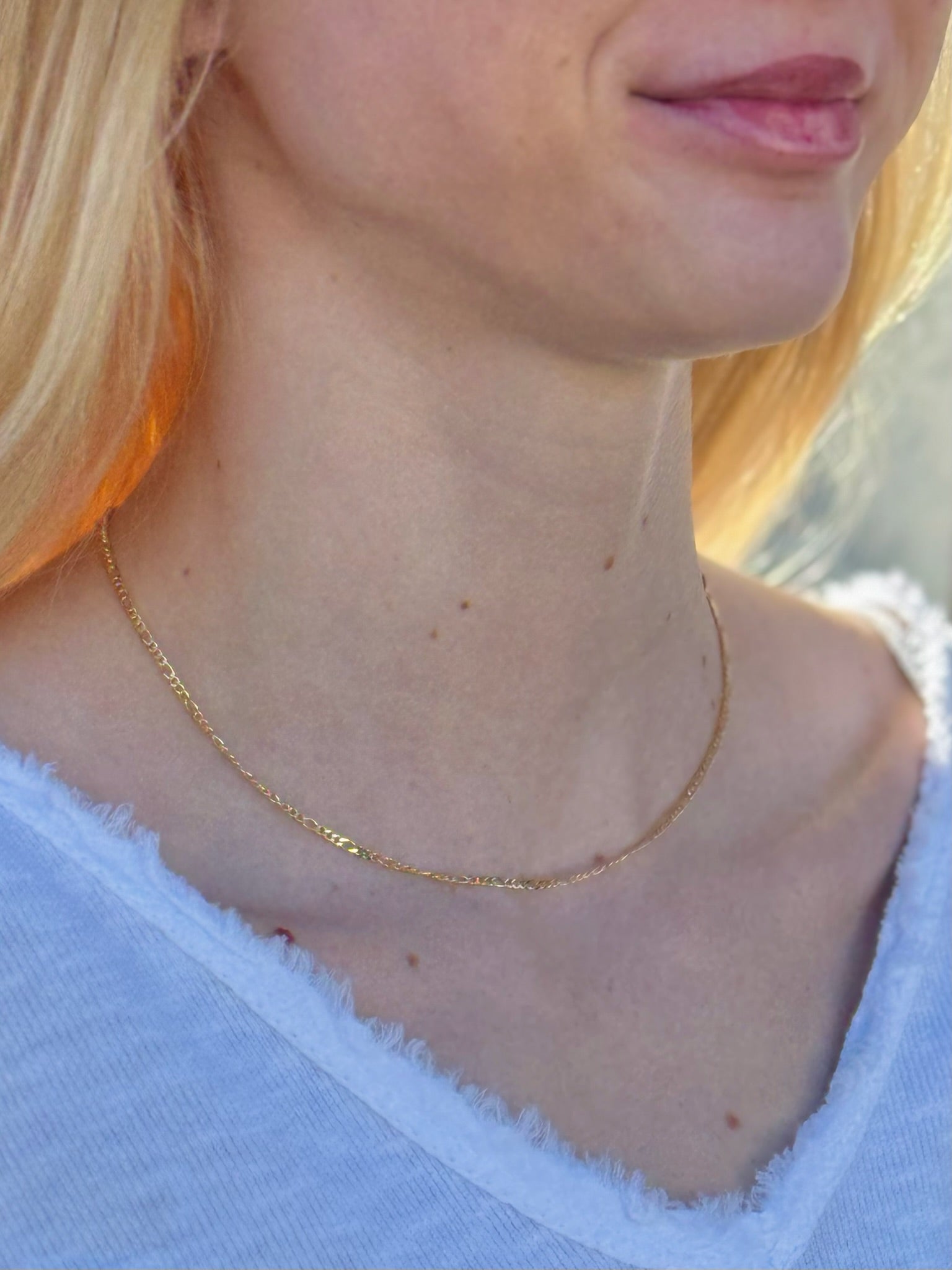 Close-up of a person wearing a gold necklace with a blurred background