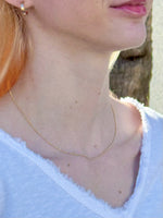 Close-up of a person wearing a delicate gold necklace with a blurred background