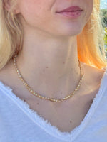 Close-up of a person wearing a gold chain necklace with a blurred background