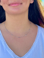Close-up of a person wearing a silver necklace with a blurred background