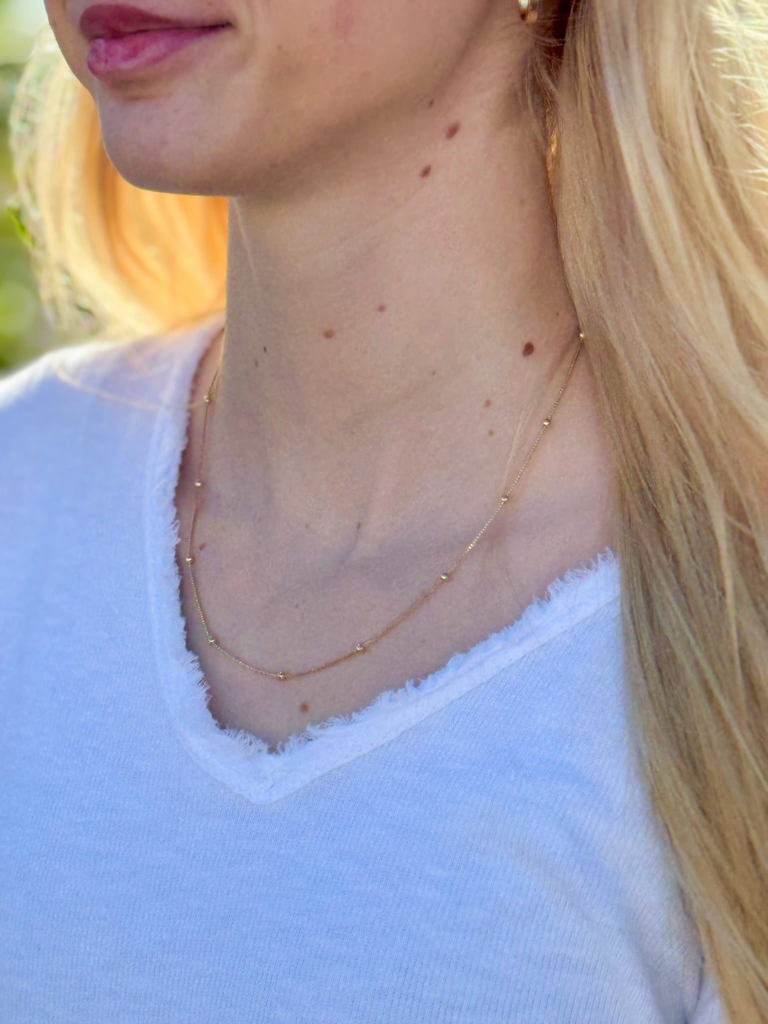 Close-up of a person wearing a delicate gold necklace with a blurred background