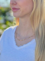 Close-up of a person wearing a gold necklace with a blurred natural background