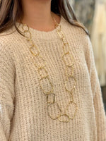 Gold chain necklace worn by a person in a beige sweater.