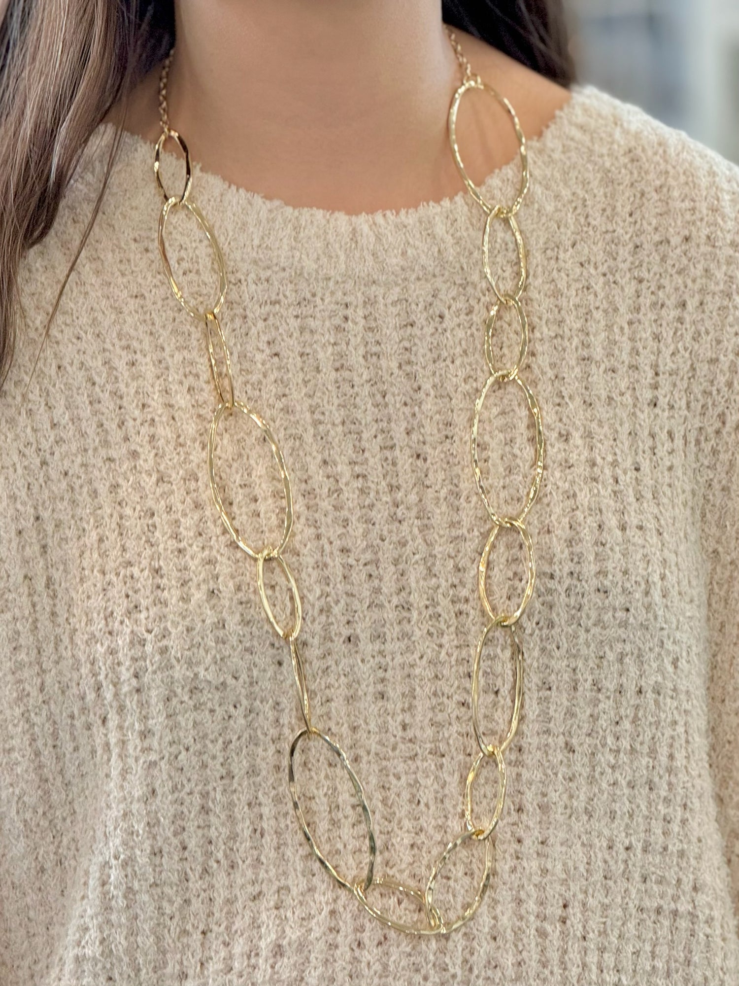 Gold chain necklace worn by a person against a neutral background