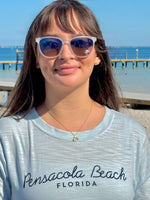 sparkly gold over sterling silver dolphin tail necklace worn on an adjustable chain, shown on model at the beach.
