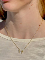 Close-up of a gold necklace with a pendant on a person wearing a beige top.