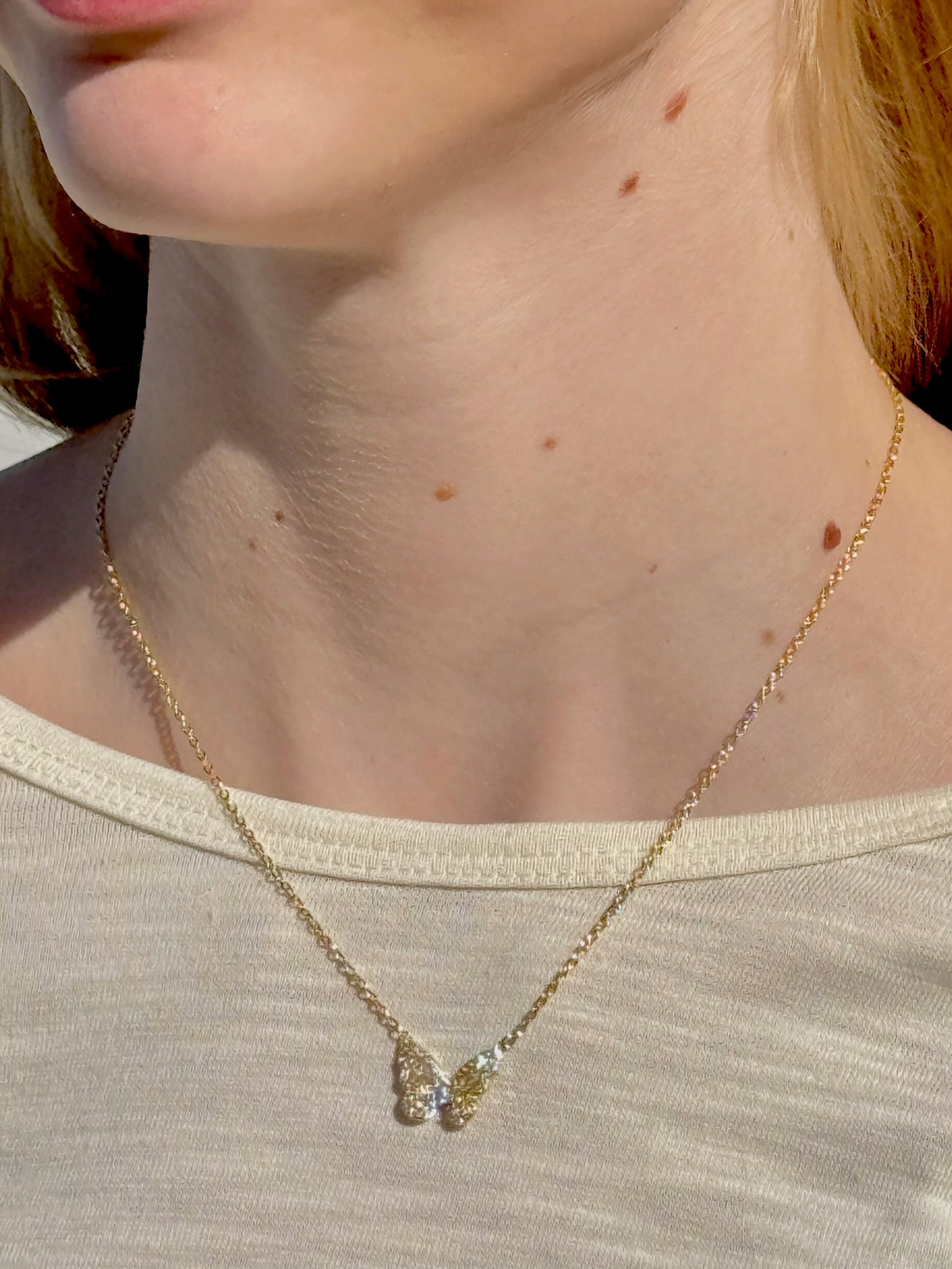 Close-up of a gold necklace with a pendant on a person wearing a beige top.