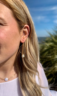 Gold dangle earring with pearl hanging from bottom center in ear