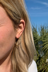 Gold hoop earrings with a knot feature on the bottom center of the earring in an ear