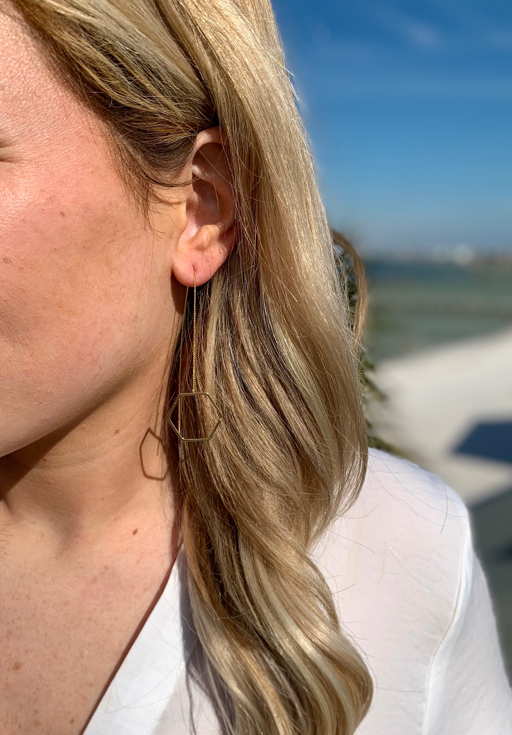 Gold dangly Octavia earrings in ear with hanging hexagon accent