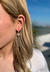 Silver mina dangle earrings in ear with a pearl accent at the top and silver dangle feature hanging below pearl