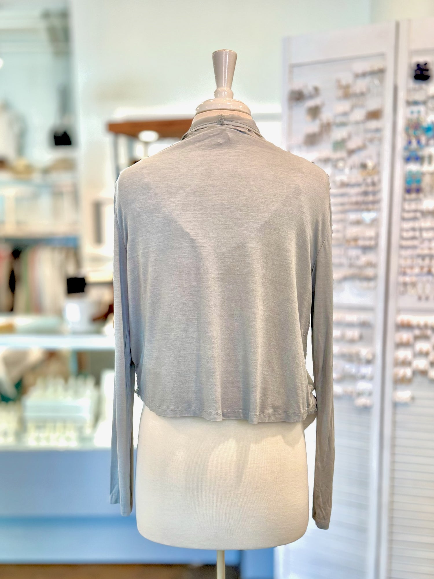 Light gray cardigan with lace detailing on a mannequin in a blurred indoor setting