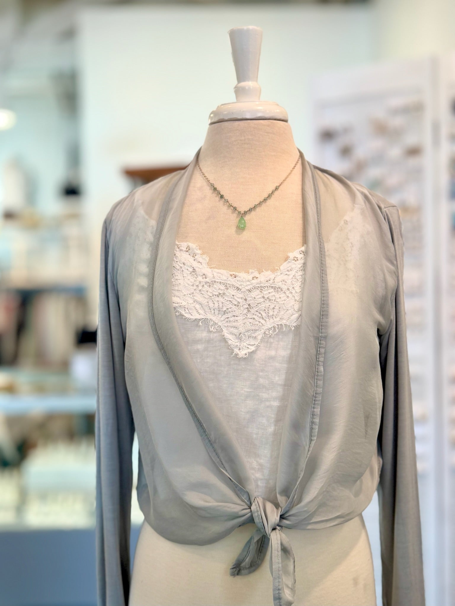 Light gray cardigan with lace detailing on a mannequin in a blurred indoor setting