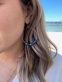 Gold hoop earrings with three blue bead details on model
