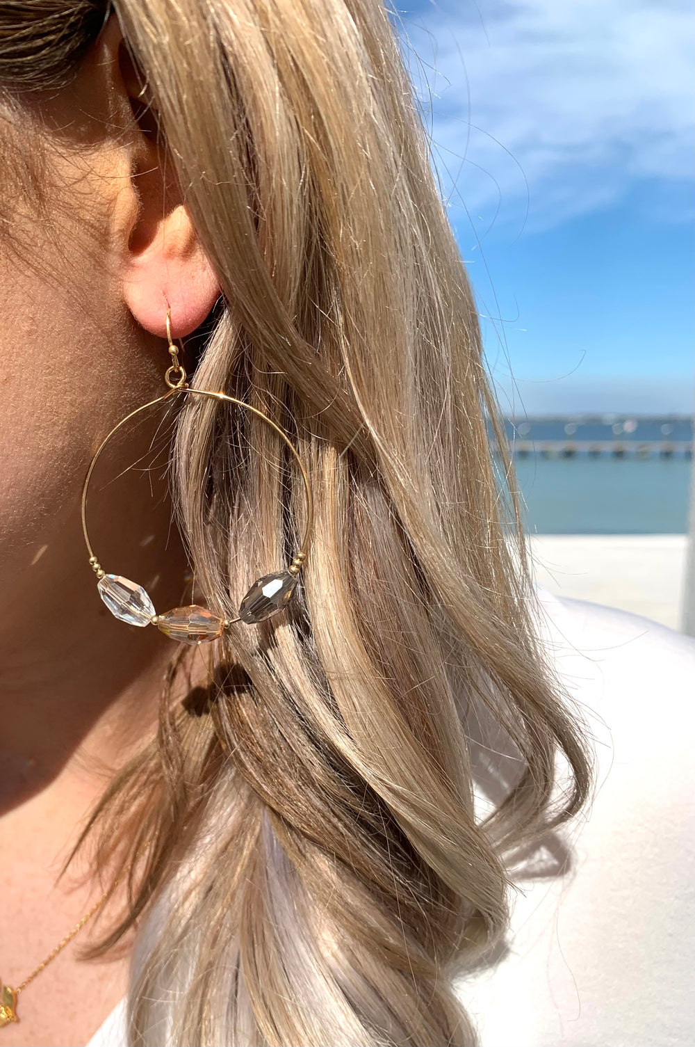 Gold hoop earrings with three beaded details with colors of clear, and different shades of brown. Photo shows earring in ear on model.
