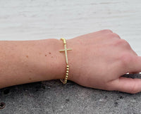 Gold beaded cross bracelet on model. 