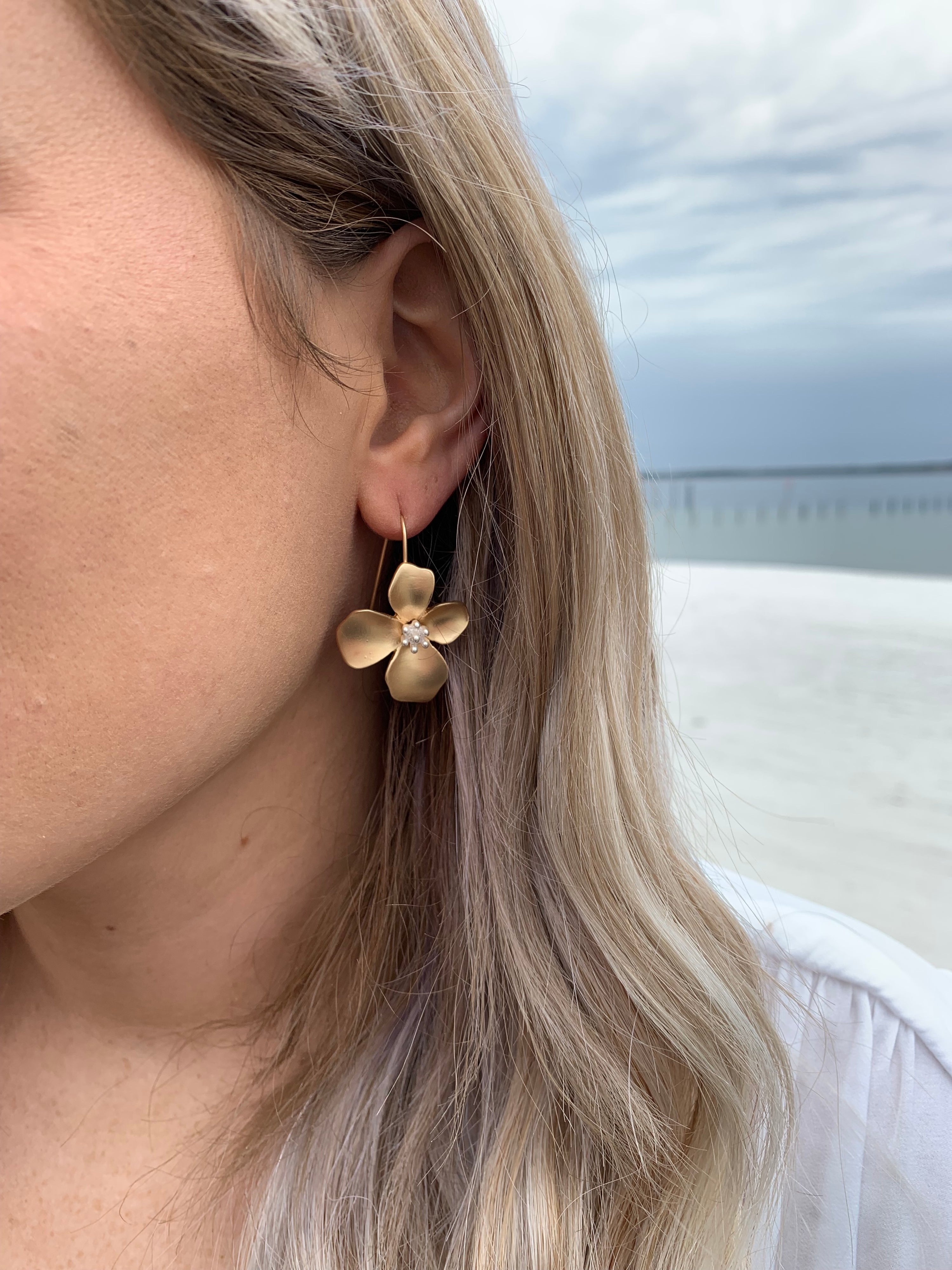 Gold magnolia flower earrings with a silver detail in the middle on model