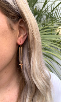Gold Noami dangle earrings in ear with cross at bottom