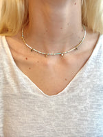 Necklace with small blue and white beads, and petite gold accents worn by a person in a light-colored top