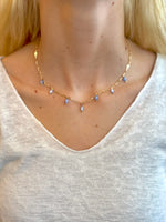 Woman wearing a gold necklace with dangling lavender bead accents, styled with a soft scoop-neck white top