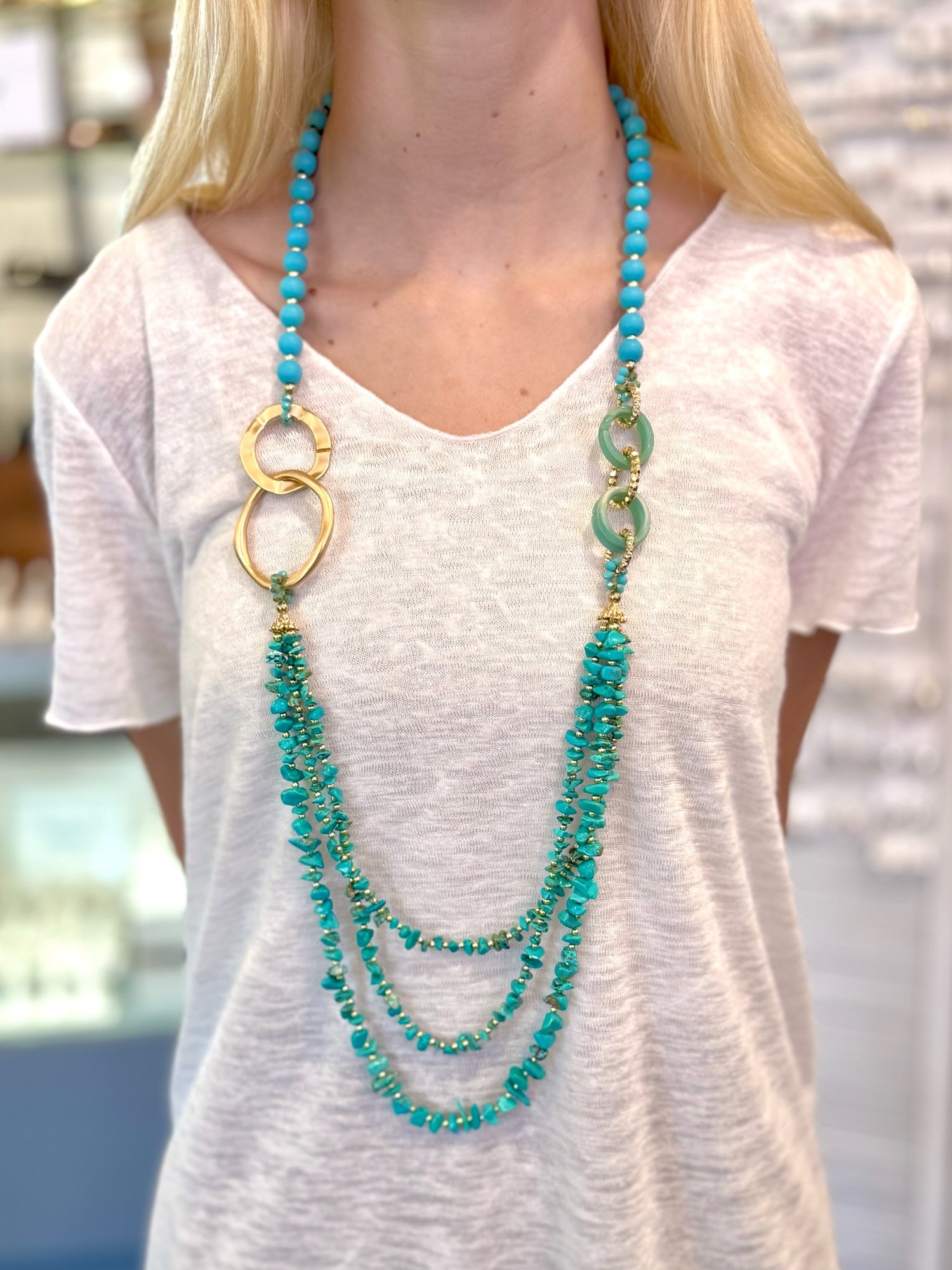 Triple-strand turquoise statement necklace with gold and resin details worn over a white top.