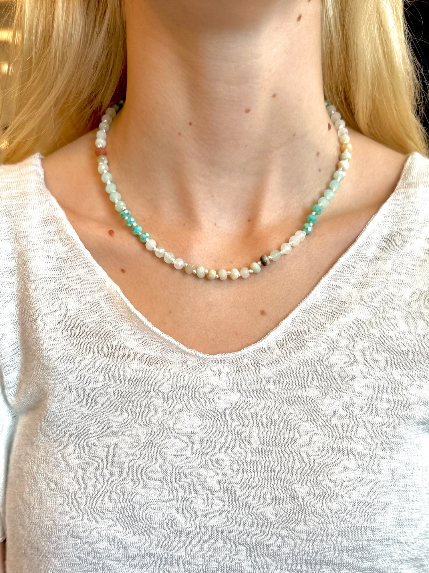 Beaded necklace with faceted aqua, jade, and pearl-toned beads and a gold extender chain, styled on a woman wearing a white top.