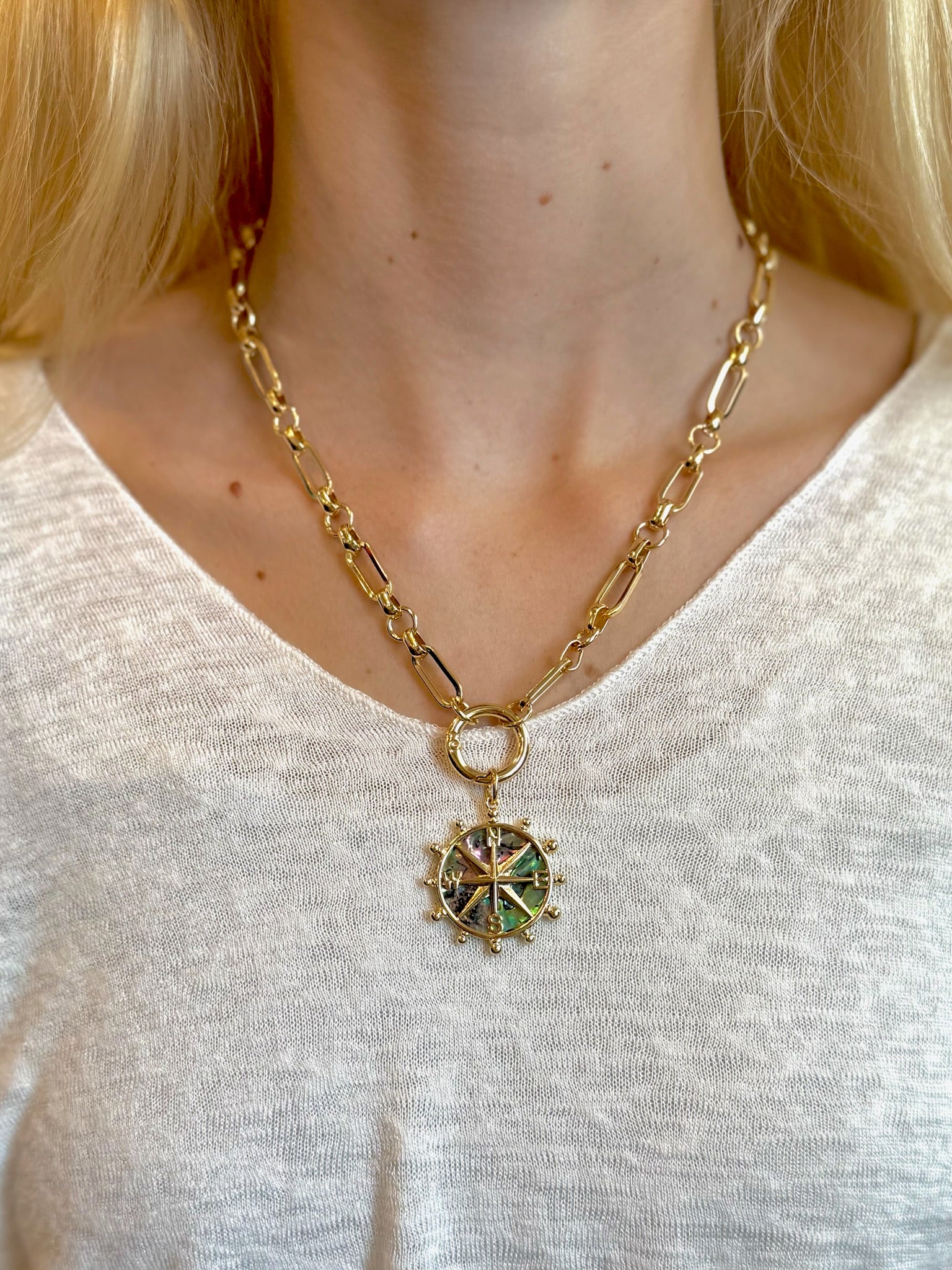 Nautical-style necklace featuring a gold chain and iridescent abalone shell compass pendant