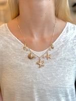 Gold necklace with starfish and shell charms worn by a person on a white background